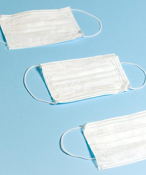 Three white face masks arranged on a pastel blue background, symbolizing health protection.